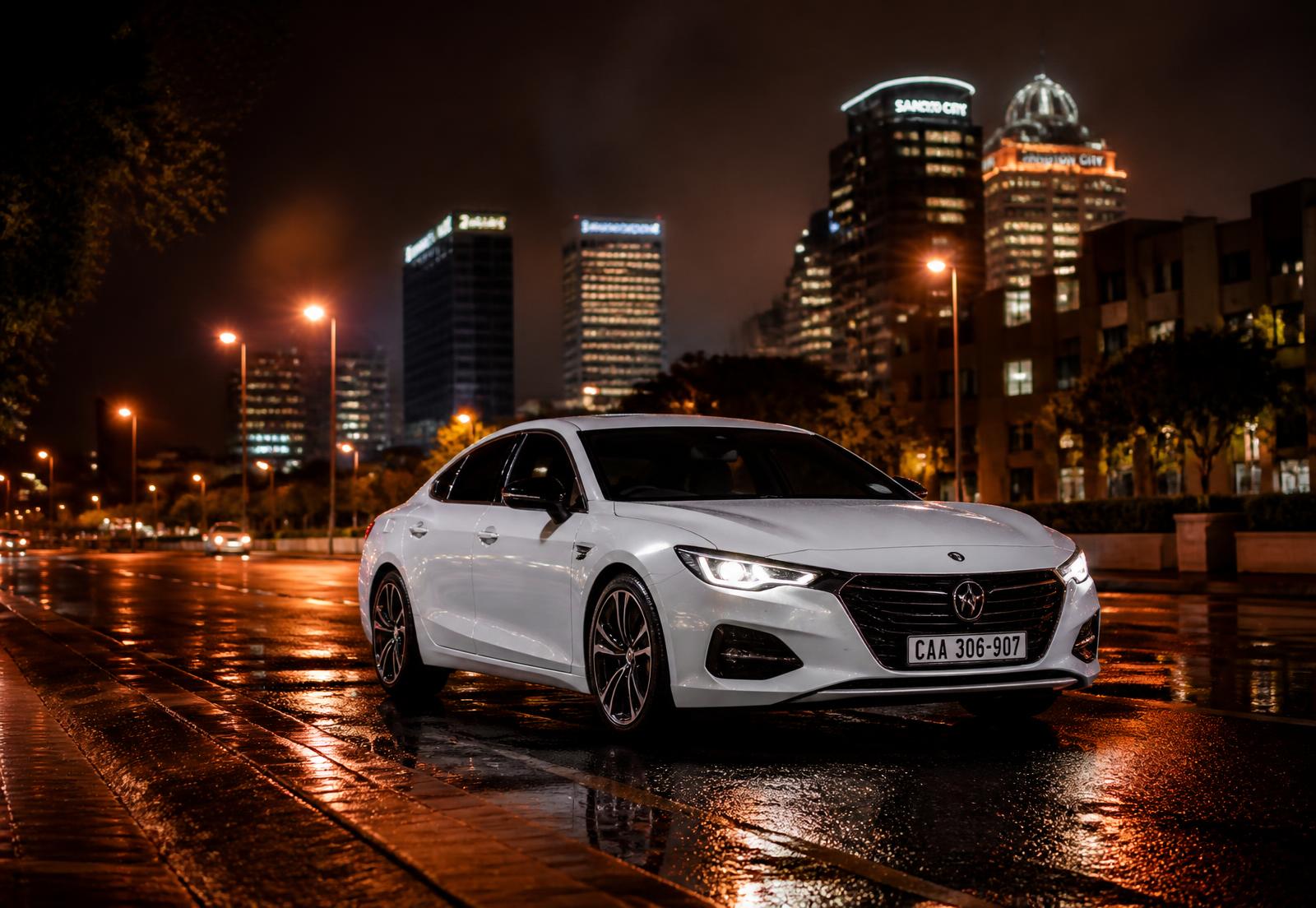 White Sift sedan on a wet Johannesburg street at night with the Sandton skyline behind it